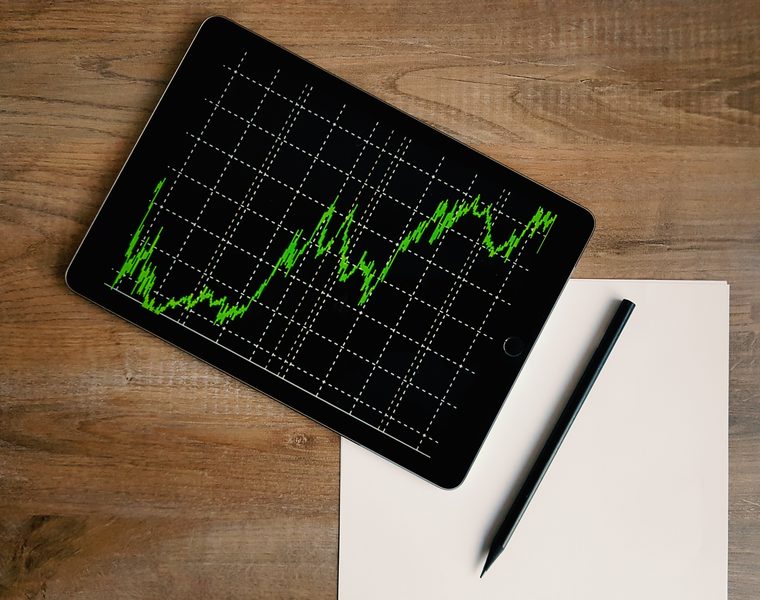 A tablet showing a rising market chart beside a notepad and pencil